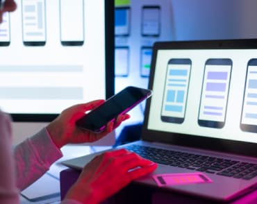person holding phone and looking at the monitor screen